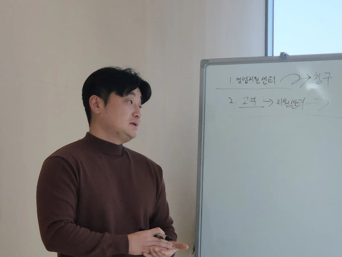 화이트보드 앞에서 영업지원센터와 청구 흐름을 설명하는 교육 장면