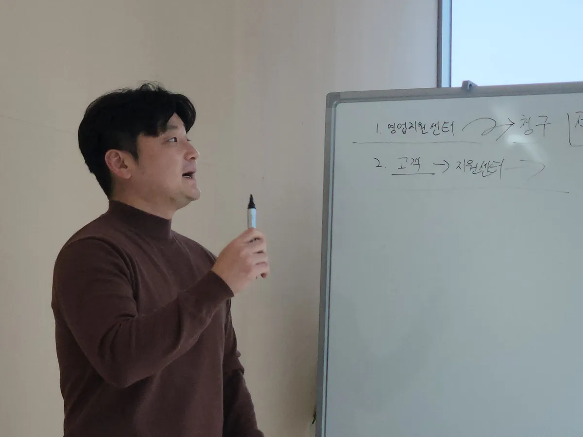 마커를 들고 고객과 지원센터의 업무 흐름을 설명하는 교육 장면